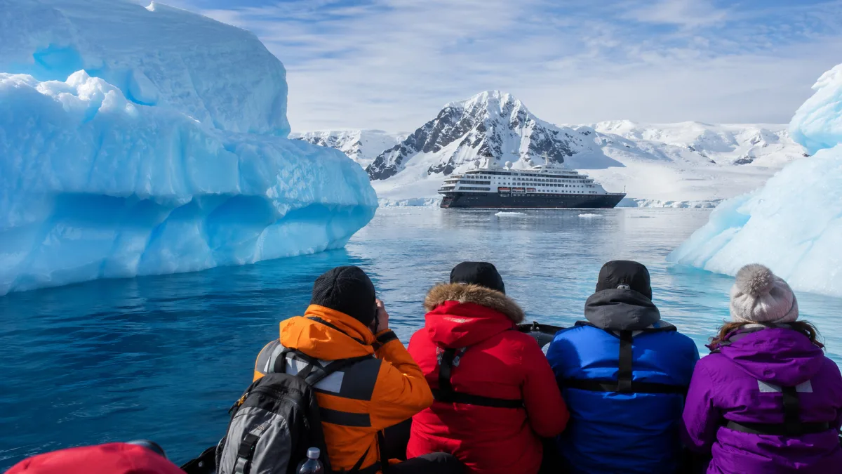 Pasajeros en zodiac entre icebergs con el barco de expedición al fondo